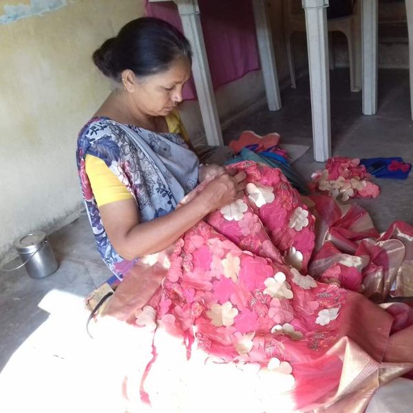 Ramiben Makwana stitching a large pink patchwork quilt decorated with appliqué flowers